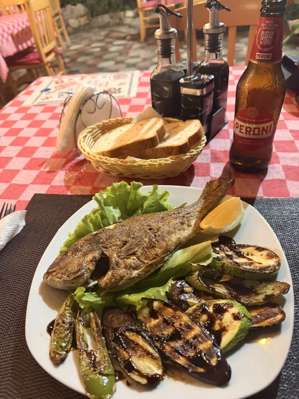 Un piatto di pesce intero grigliato con verdure grigliate e una birra in un ristorante a Valona, Albania.