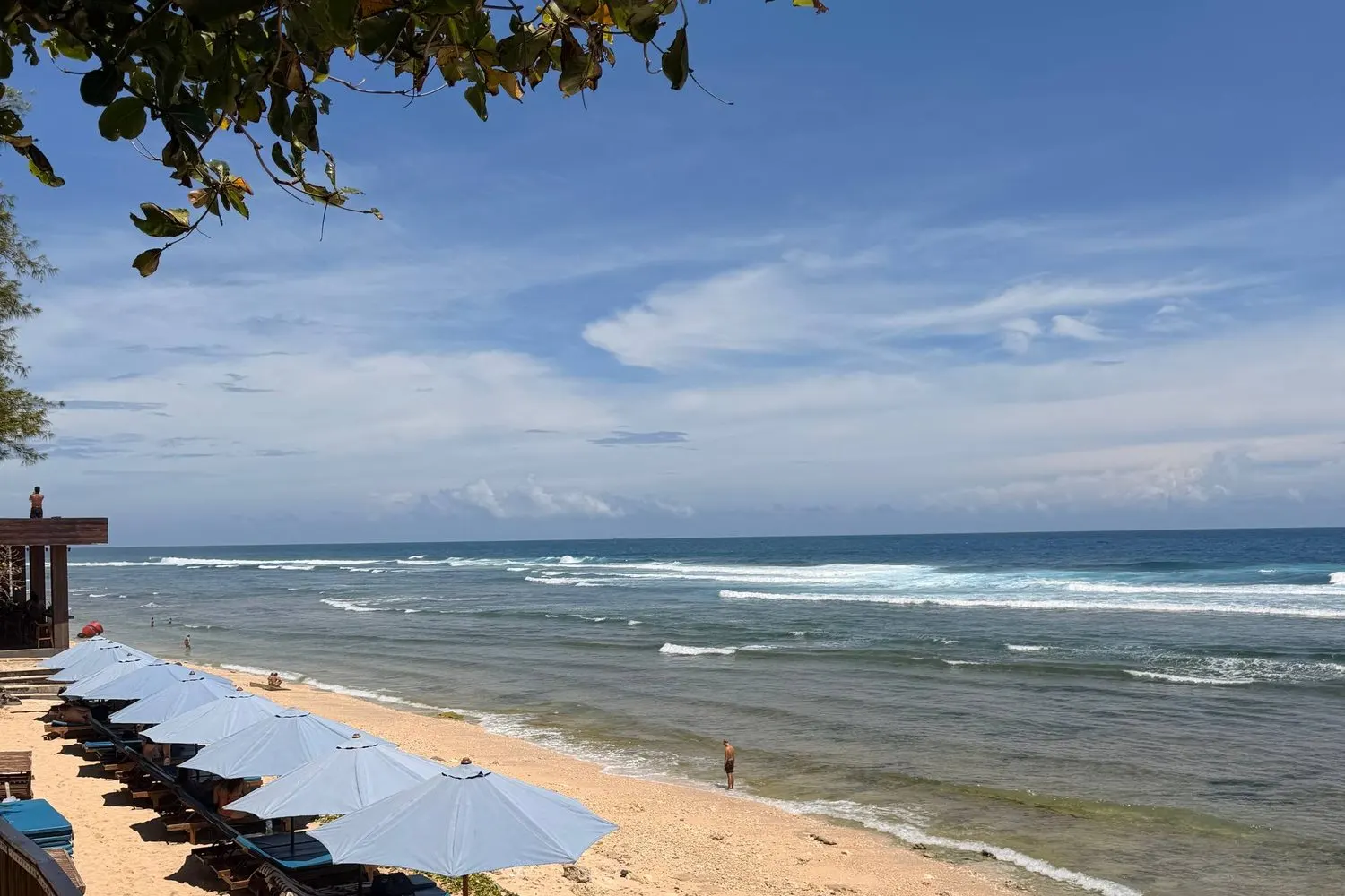 Un beach club a Bali con ombrelloni azzurri sulla sabbia dorata e le onde, vicino a Canggu.