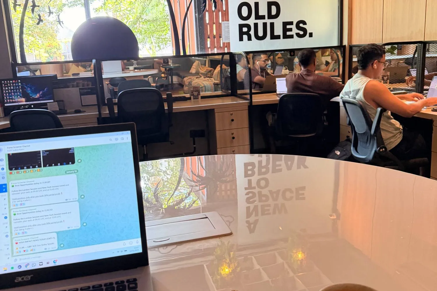 A coworking space in Bali, a laptop and coffee in the foreground, people working behind.
