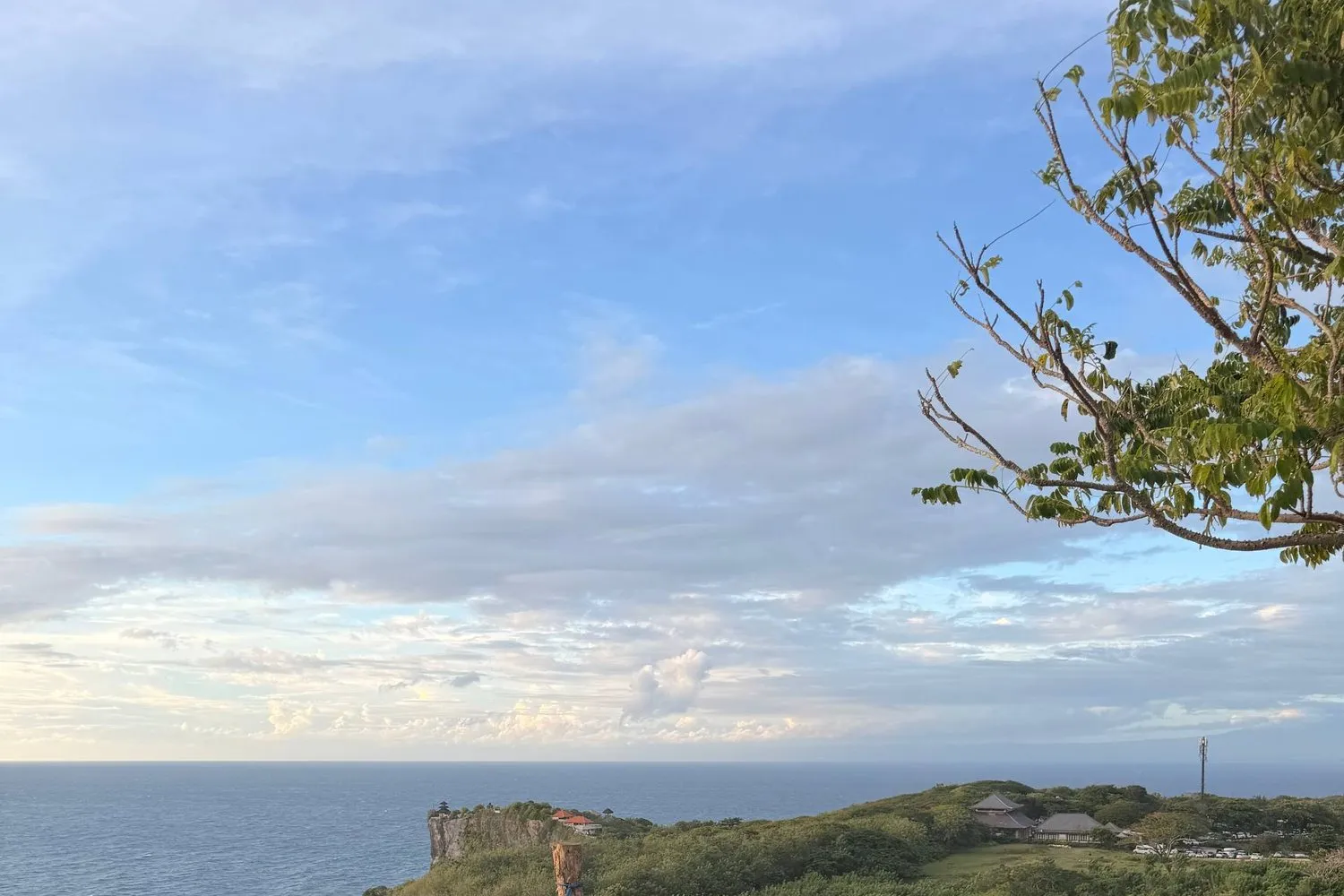 La costa a strapiombo di Uluwatu, Bali, con l'oceano sotto e un tempio sul promontorio verde.