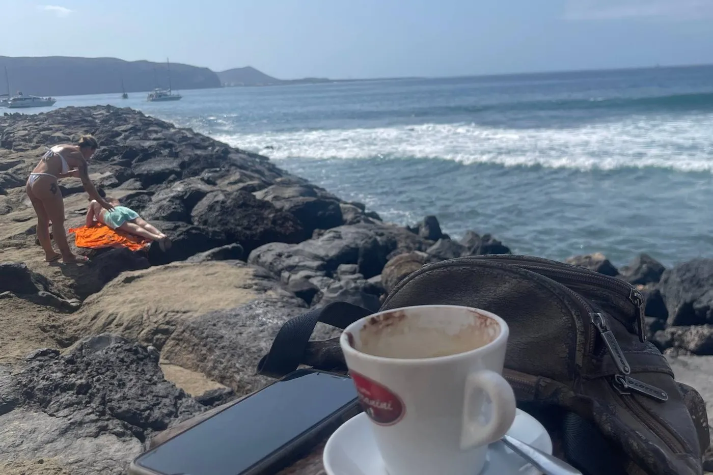 A coffee and a phone resting on a rock by the sea, the quiet weekly ritual of checking how a site is doing.
