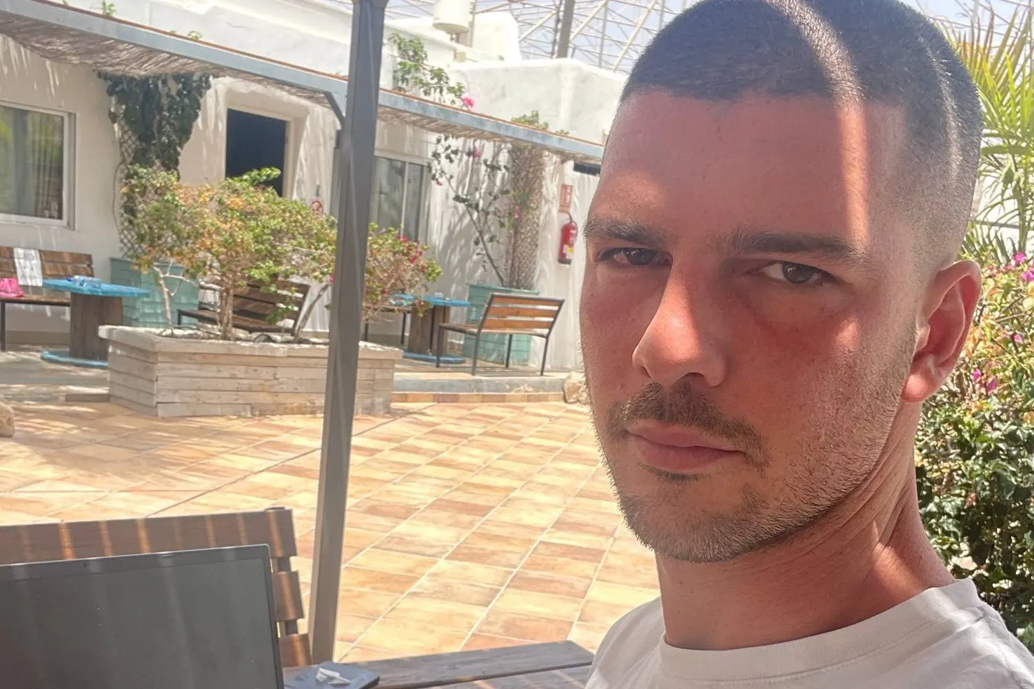 Marco Nicola Messina working from a sunny terrace abroad, a laptop on the table.